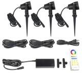 AuraLed Smart Garden Spotlight Kit contents laid flat, including three black spike-mounted spotlights with cables, a power supply unit, connectors, and an RF colour remote control